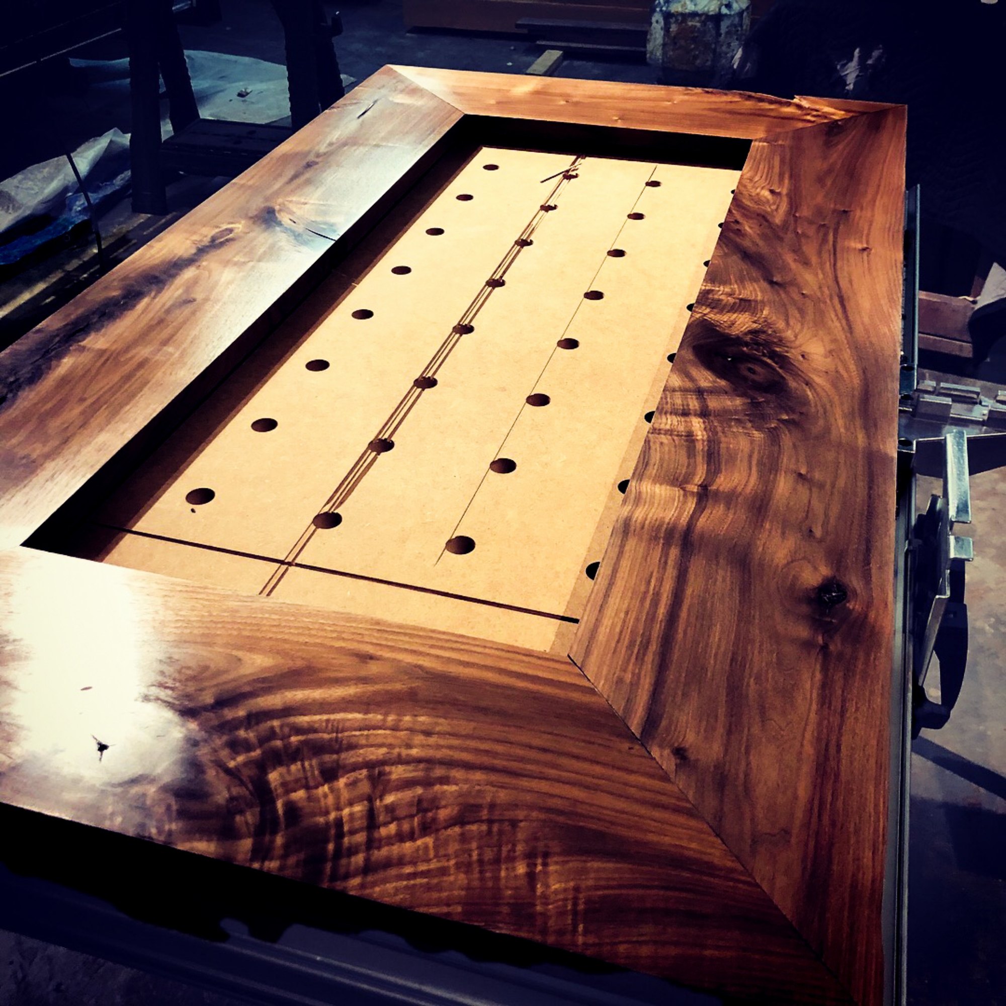 A mitered walnut table top awaiting its glass inset, mirror-deep finish