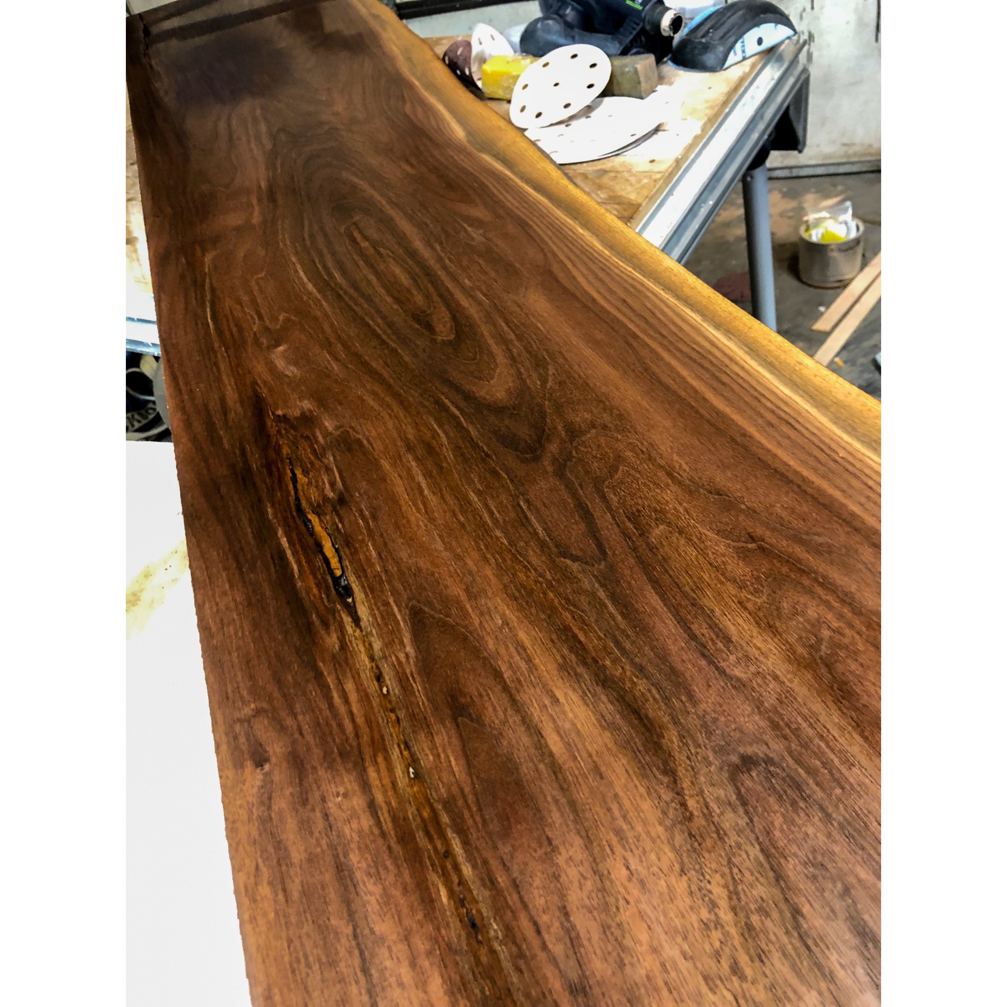 The walnut slab on the bench mid-finishing, sanding discs behind